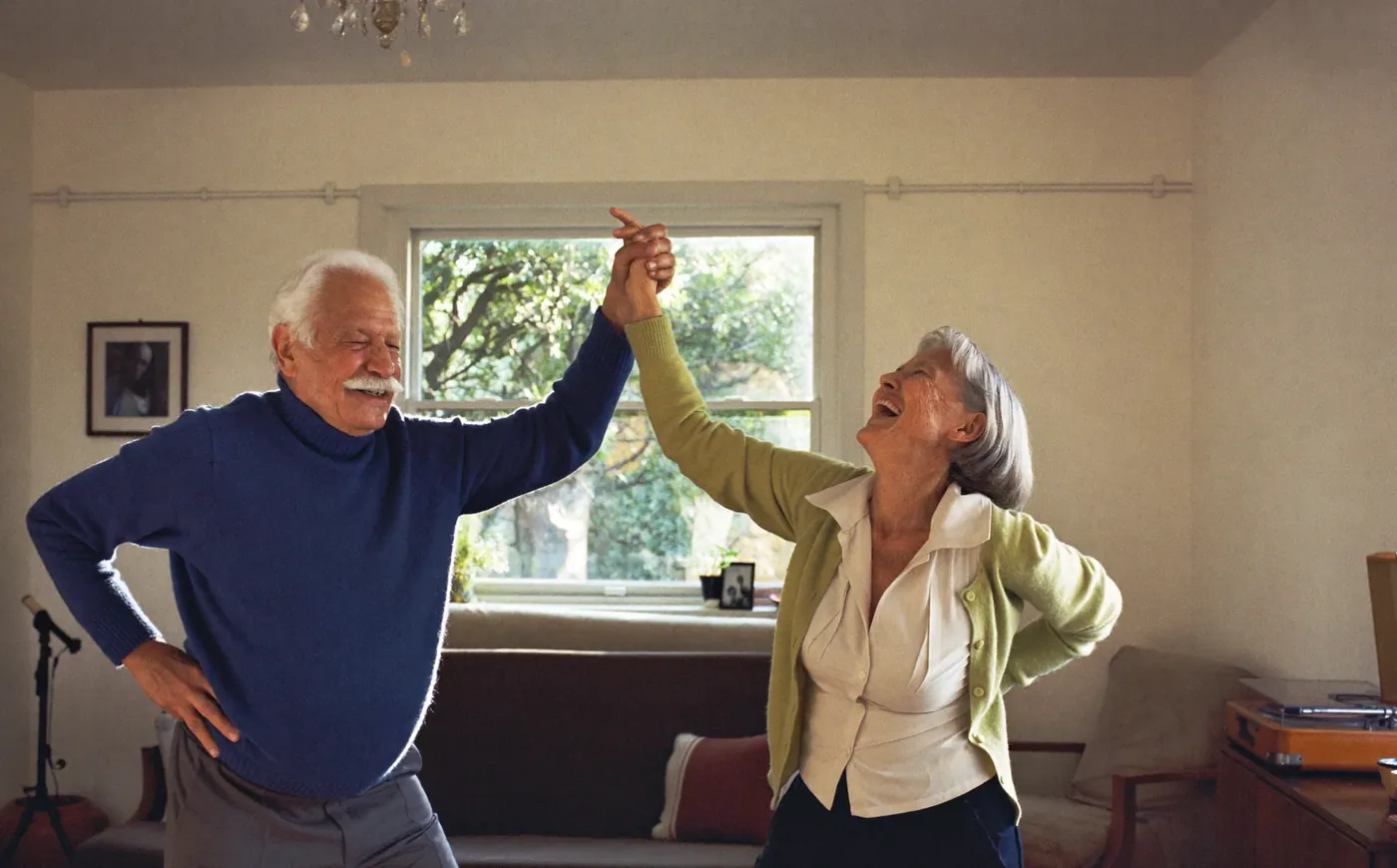 Una pareja de personas mayores baila riendo en su living